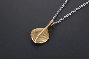 Macro shot of vintage gold feather pendant on silver chain necklace showing vein texture