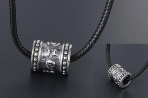 Macro shot of titanium steel cylinder pendant with engraved Buddhist mantra and retro finish