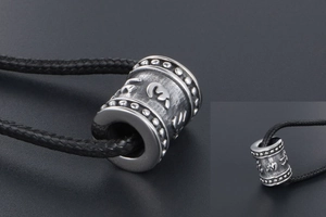 Macro detail of silver cylinder pendant with engraved Buddhist mantra and woven cord