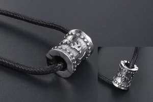 Détail macro du pendentif cylindre en titane argenté avec symboles de mantra gravés