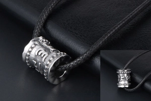 Gros plan du pendentif cylindrique en titane avec caractères de mantra religieux