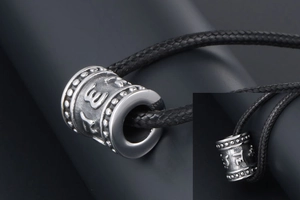 Close-up of titanium steel cylinder pendant with engraved mantra and braided rope
