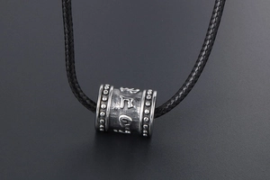 Macro shot of titanium steel cylindrical pendant featuring engraved Buddhist mantra characters