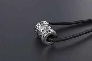 Macro shot of silver barrel pendant with engraved mantra and black braided cord
