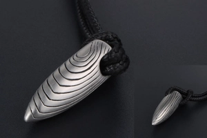 Détail d'un pendentif balle en argent mat avec texture brossée et cordon noir tressé