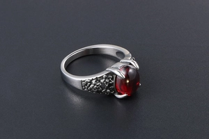 Detail of vintage silver ring with red gemstone and floral engravings on band