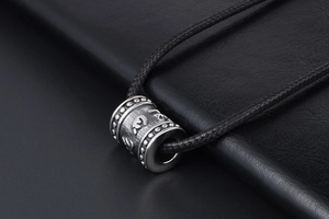Macro shot of titanium steel cylinder pendant with embossed six-word mantra details