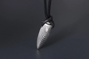 Détail du pendentif balle en argent avec motifs annelés et cordon noir tressé