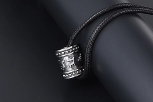 Macro shot of titanium steel cylinder pendant with mantra engraving and woven cord