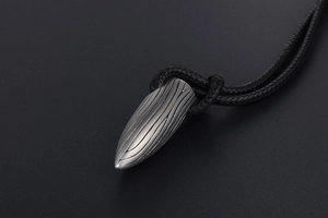 Vue détaillée du pendentif balle en argent mat avec rainures verticales sur fond noir