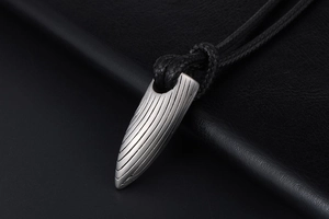 Gros plan du pendentif balle argent mat avec texture brossée sur fond en cuir noir