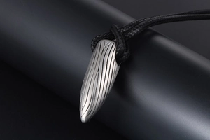 Macro d'un pendentif balle en acier inoxydable avec lignes texturées et cordon tressé