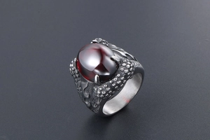 Macro shot of gothic dragon claw ring with deep red oval gemstone and scaly metal texture