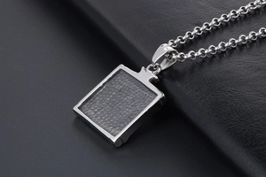 Macro detail of square stainless steel pendant with dark textured inlay on black leather