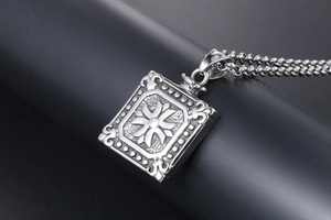 Detailed close-up of a silver rectangular pendant with embossed floral patterns on a bead chain