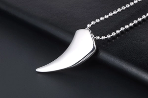 Détail d'un pendentif dent de loup poli sur chaîne à billes sur fond de cuir noir texturé