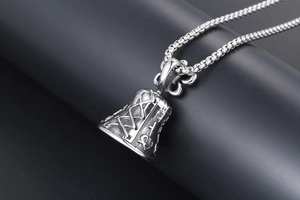 Detail of vintage bell pendant with engraved cross on a thick square pearl chain