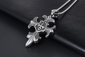 Vue macro du pendentif croix gothique argentée avec motifs de lys et relief en bouclier