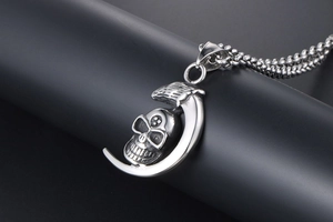 Macro shot of stainless steel crescent moon and skull pendant on a black prop
