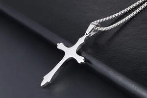 Macro shot of a silver titanium steel cross pendant on a black leather texture background