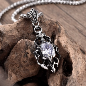 Gothic flame-shaped stainless steel necklace with a sparkling oval gemstone pendant on wood