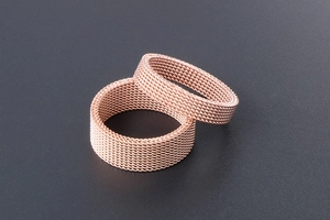 Macro shot of rose gold mesh woven rings in wide and narrow widths on a grey background