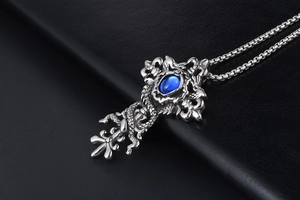 Macro shot of gothic cross pendant with blue gemstone and detailed dragon wrap carving