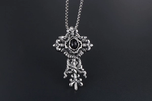Macro view of silver Gothic cross pendant featuring intricate carving and black stone inlay