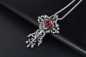 Detail of gothic silver cross pendant featuring a red stone and intricate snake relief