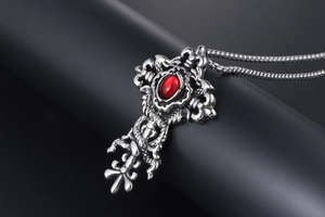 Detail of gothic cross pendant with red gemstone and silver snake chain on a black stand