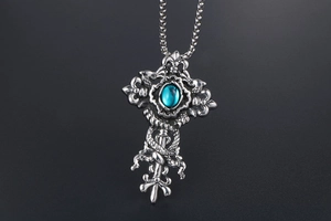 Macro detail of gothic cross pendant with blue gemstone and fleur-de-lis engravings