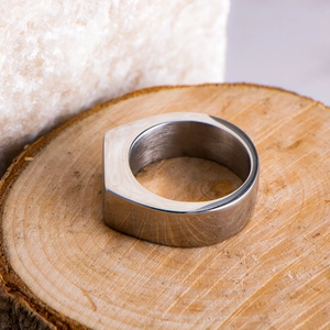 Close-up of minimalist rectangular silver titanium ring on a natural wood surface