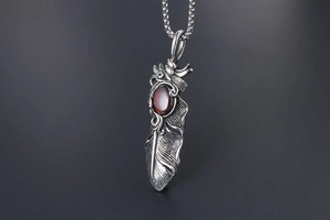 Macro detail of retro steel feather pendant with deep red oval gemstone on textured metal chain
