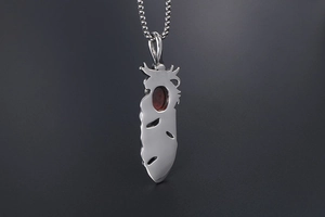 Detailed close-up of a silver feather pendant featuring a polished red ruby gemstone inlay