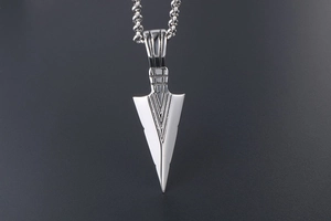 Macro detail of polished silver arrow pendant with geometric V-shaped engravings