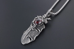 Detailed macro view of vintage silver feather pendant with a deep red ruby gemstone inlay
