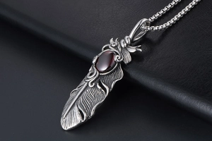 Detailed close-up of a silver feather pendant featuring a deep red oval gemstone inlay