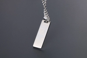 Macro view of rectangular brushed steel pendant with modern box chain on grey texture