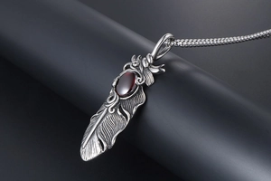 Macro detail of silver titanium feather pendant with oval red gemstone and vintage texture