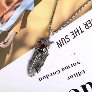 Retro feather pendant necklace in silver with red gemstone on fashion magazine background