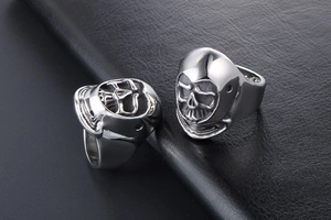 Close-up of two gothic silver skull rings on a black leather texture background