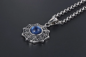 Détail du pendentif en acier vintage avec pierre bleue et gravure sur sable noir