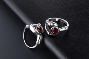 Macro detail of gothic claw rings with red faceted gemstones on black leather background