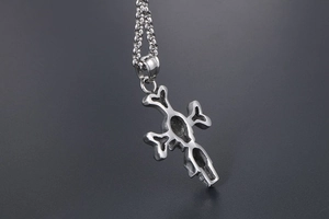 Close-up of vintage punk cross pendant featuring dual skulls and silver steel chain