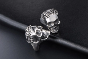 Macro view of two silver skull rings with ornate floral engravings in punk rock style