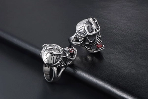 Detailed view of two silver skull rings with red gemstones on black leather background