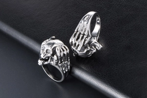 Macro shot of silver skull ring and skeletal hand band on black leather surface