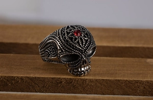 Macro shot of silver skull ring with red gemstone eye and embossed dotted metal detail