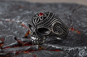 Detailed close-up of a vintage silver skull ring with a red gemstone on dark rock