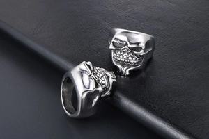 Close-up of two punk style stainless steel skull rings with brushed finish on black leather